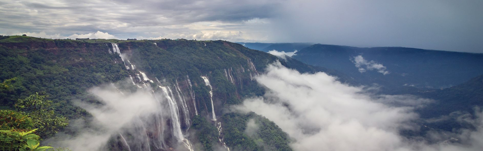 Panoramic view of a nohkalikai falls cascading into a deep gorge with clouds below.